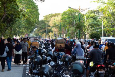 24 Ağustos 2024 'te Mataram, Lombok, Endonezya' da bir halk etkinliği sırasında büyük bir insan ve motosiklet kalabalığı ağaç sıralı bir caddeyi kuşatıyor.