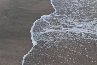 Koyu kahverengi kumla buluşan desenli beyaz okyanus köpüğünün yakın görüntüsü