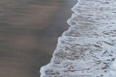 Koyu kahverengi kumla buluşan desenli beyaz okyanus köpüğünün yakın görüntüsü