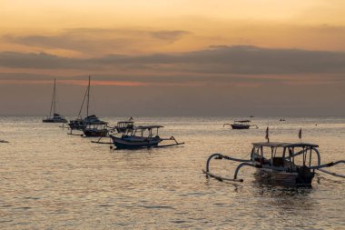 Geleneksel Endonezya tekneleri gün batımında altın okyanusta huzur içinde yüzerler.