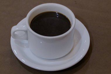 Klasik Beyaz Seramik Kupa. İçi bir fincan çay tabağında sıcak koyu kahveyle dolu.