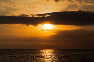 Altın gün batımı ışığı dramatik bulutların altındaki karanlık okyanus dalgalarına güzel bir şekilde yansıyor.