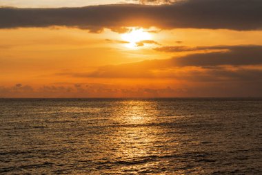 Altın gün batımı ışığı dramatik bulutların altındaki karanlık okyanus dalgalarına güzel bir şekilde yansıyor.
