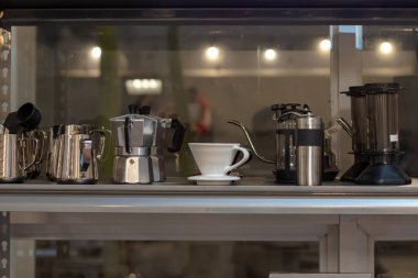 Kafedeki bir rafta düzgünce sergilenen çeşitli kahve demleme aletleri koleksiyonu
