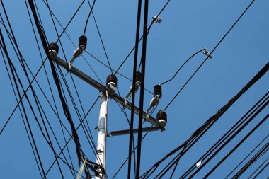 Açık mavi gökyüzüne karşı kablolar ve elektrik hatlarından oluşan karışık bir ağ.