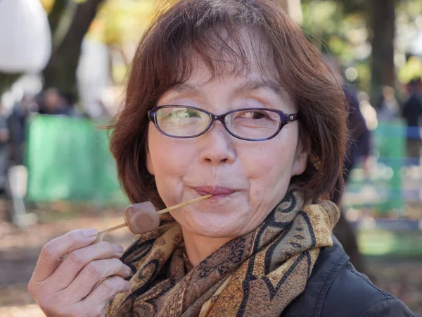 An older Japanese woman eating dango outside