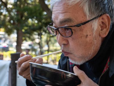 Yaşlı bir Japon yemek çubuklarıyla yemek yiyor..