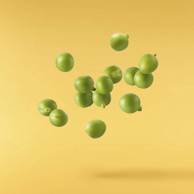 Taze çiğ bezelyeler sarı arka planda izole bir şekilde havaya düşüyorlar. Gıda havalanması veya sıfır yerçekimi kavramı