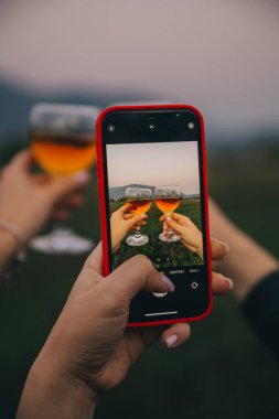 Kadınlar ellerinde şarap kadehleriyle akıllı telefonlarıyla fotoğraf çekiyorlar.