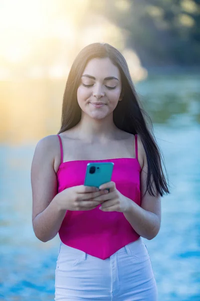 スマートフォンでヨーロッパのティーンエイジャー 背景がぼやけている ピンクのシャツを着たロングヘア ストック写真