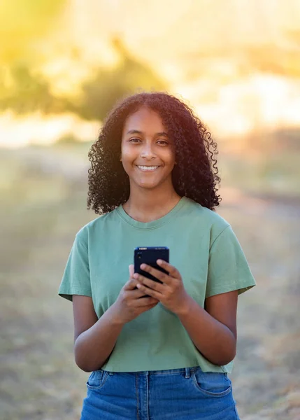 夏の日の間にスマートフォンを使用して巻き毛を持つ美しい笑顔の女の子 — ストック写真