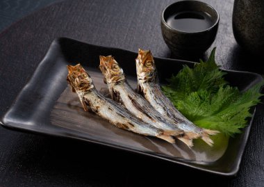 Grilled urume sardines on a black table. A side dish of sake. Japanese food image.