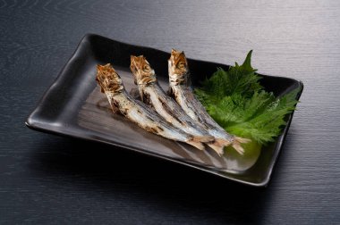 Grilled urume sardines on a black table. A side dish of sake. Japanese food image.