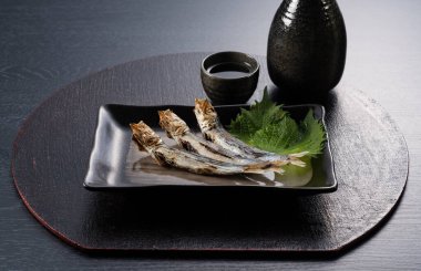 Grilled urume sardines on a black table. A side dish of sake. Japanese food image.