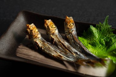Grilled urume sardines on a black table. A side dish of sake. Japanese food image.