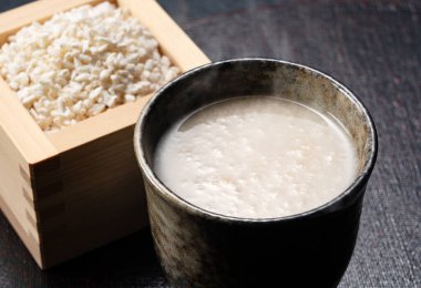 Amazake placed against a black background and rice koji in a masu box. Amazake is a traditional Japanese sweet drink. Koji is fermented rice. 