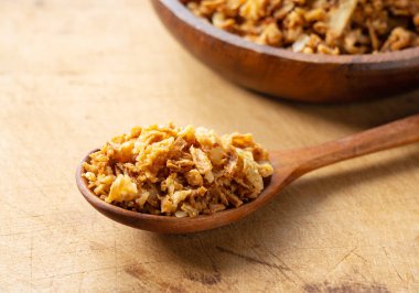 Fried onions and wooden spoon on wooden background. Crispy fried onions. 