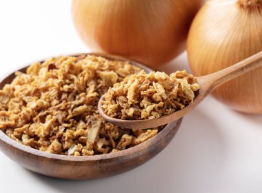 Fried onions and wooden spoon in bowl on white background. Crispy fried onions. 