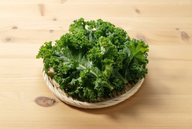 Ahşap arka plana yerleştirilmiş bir kevgirde kale. kıvırcık lahana.