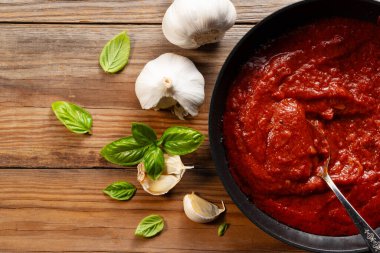Kızartma tavasında domates sosu. Fesleğen ve sarımsak var. Doğrudan yukarıdan bak. Ahşap arkaplan.