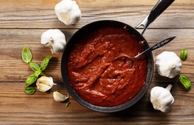 Kızartma tavasında domates sosu. Fesleğen ve sarımsak var. Doğrudan yukarıdan bak. Ahşap arkaplan.