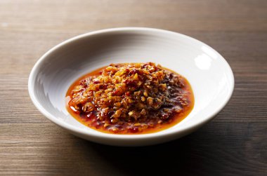 Ahşap arka planda seramik bir tabakta yenilebilir bir biber yağı..