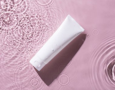 Pembe su arka planında makyaj kremi ya da losyon şişesi. .