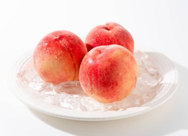 Japon şeftalilerini ve buzu beyaz arka planda bir tabakta kes. Japon şeftalilerinin resmi.