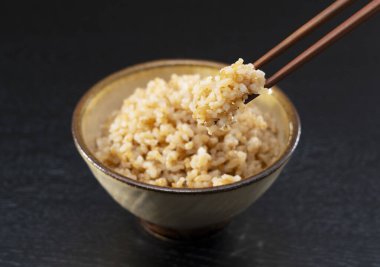 Taze pişmiş esmer pirinç, siyah arka planda, çubuklarla kaldırıldı.