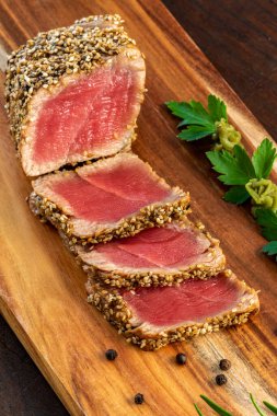 İştah açıcı susamlı, kabuklu ton balıklı tataki. Orta pişmiş sarı yüzgeçli ton balığı dilimleri ahşap tahtada wasabi ile.