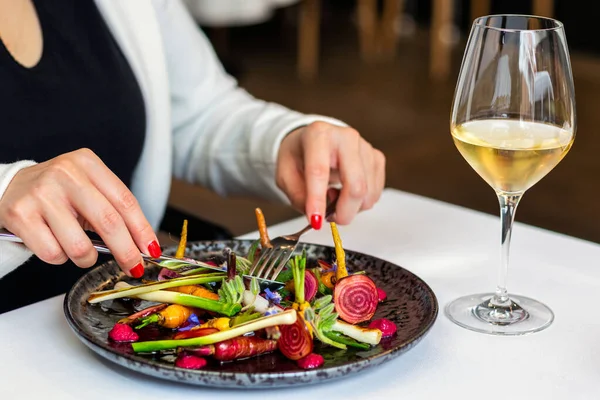 グルメレストランで新鮮な野菜のサラダを食欲をそそる女性の詳細を閉じます 皿の横にあるテーブルの上の白ワイングラス — ストック写真