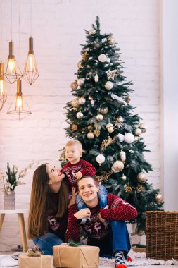 Ebeveynler ve küçük oğlu güzel bir Noel ağacının ve hediyelerin yanında oturuyorlar. Aile görünüşü.