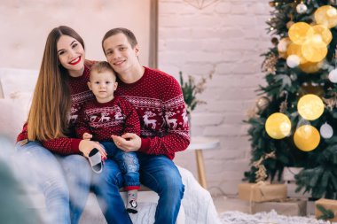 Mutlu bir aile yatakta oturup kameraya bakar. Noel ağacı yatağın yanında. Aile görünüşü. 