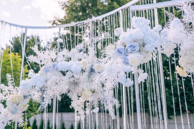 Açık havada düğün hazırlığı, pastel mavisi çiçeklerle süslenmiş düğün kemeri.