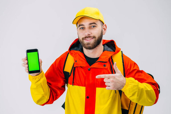 Food delivery. courier holding a mobile phone with a blank screen for mock-up, wearing a yellow cap, uniform and thermal backpack, showing thumbs up.