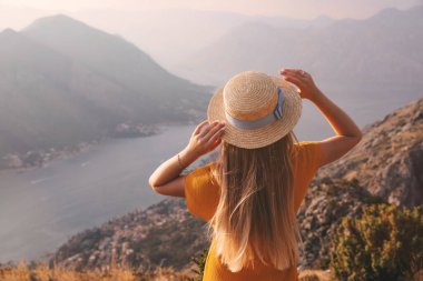 Hasır şapkalı genç kadın, yukarıdan Kotor şehrine ve Karadağ 'ın Boka Körfezi' ne bakıyor..