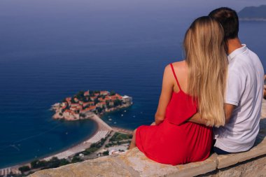 Rear view romantic young couple in love over sea shore above Sveti Stefan island in Budva, Montenegro. Travel. Vacation. Family.