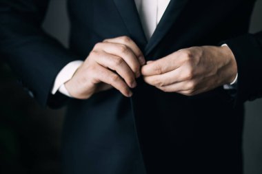 Düğünden önce damadın elleri ceketini bağlar. Siyah takım elbiseli bir adamın yakın çekimi.