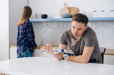 Huysuz ev hanımı arkada dikilip alkolik kocasını izliyor. Bir erkek ve bir kadın, erkek alkolizmi nedeniyle ev mutfağında anlaşmazlık yaşıyor. İlişki ve evlilik sorunları