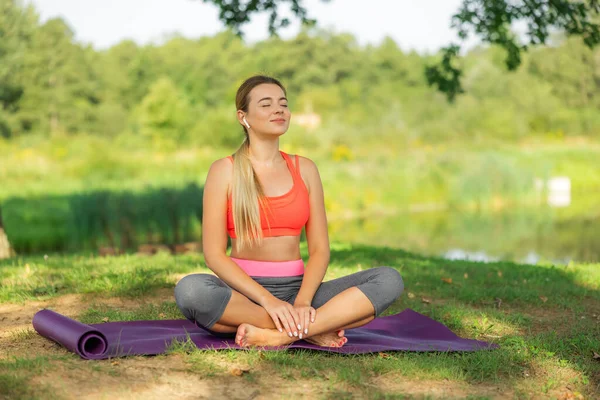 Close up portrait of smiling woman in sporty outfit relaxing meditating feeling zen-like on fitness mat in public park outdoors. Healthy active lifestyle