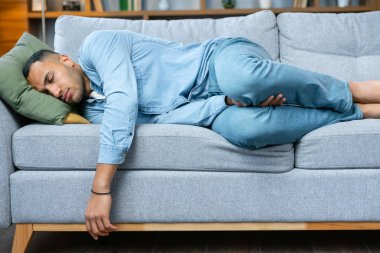 Side view of a young handsome bearded man in casual clothes sleeps on the couch in a room at home.