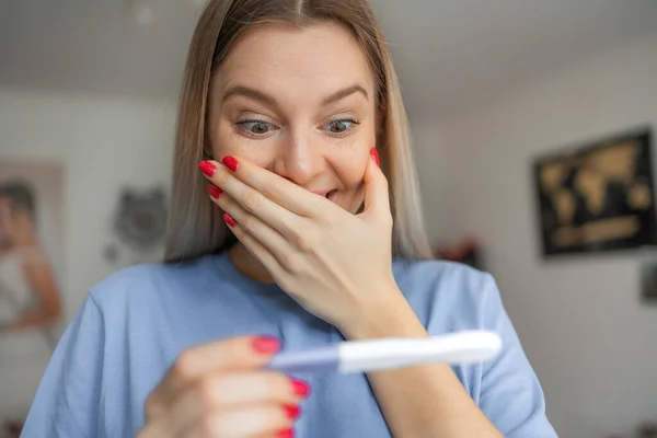 Happy smiling woman looking at pregnancy test at home. Pregnancy, fertility, maternity, emotions and people concept .