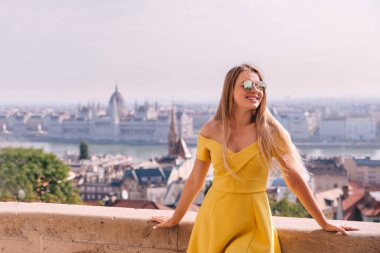 Genç sarışın bir turist, Macaristan 'ın Budapeşte kentindeki tarihi Parlamento binasının önünde poz veriyor.