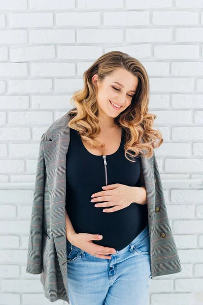 幸せな笑顔美しいです妊娠中の女性立っている彼女の腹に触れます上の青の背景 — ストック写真