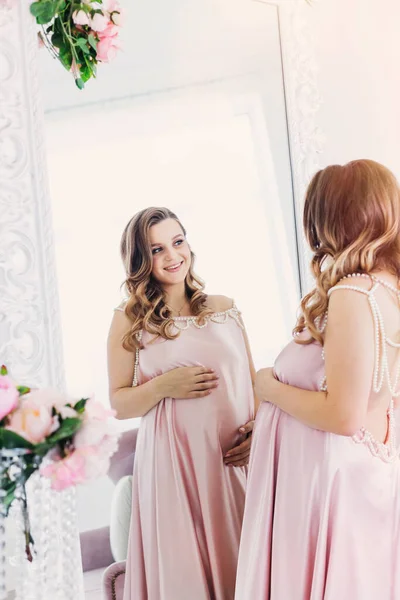 Een Gelukkige Zwangere Vrouw Een Delicate Roze Jurk Kijkt Spiegel — Stockfoto