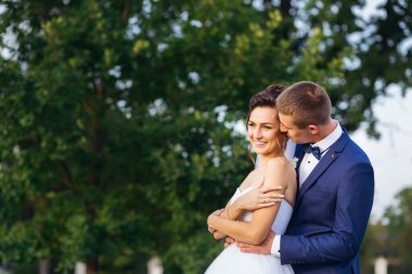 Mutlu aile gelini ve damat düğün gününde doğada birbirine sarılıyor.
