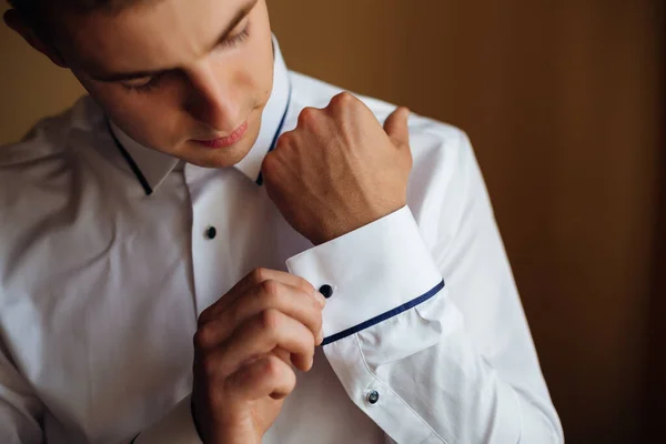 A young man is engaged, a businessman is preparing for a holiday or a business meeting. He puts on a white shirt and fastens his cufflinks