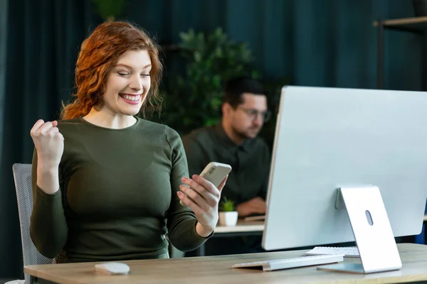 비지니스 여성은 사무실에서 일하는 컴퓨터 승리와 성공을 축하하는 스마트폰에서 소식을 — 스톡 사진