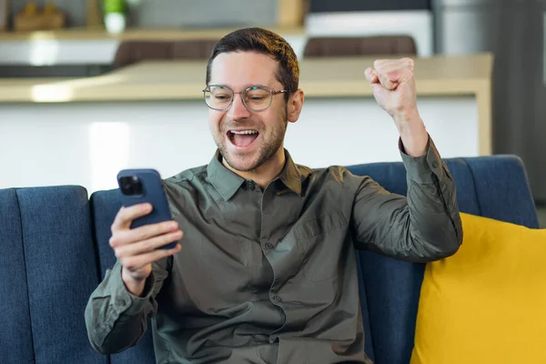 Akıllı Telefon Kullanan Genç Bir Adam Evdeki Kanepede Mutlu Heyecanlı — Stok fotoğraf