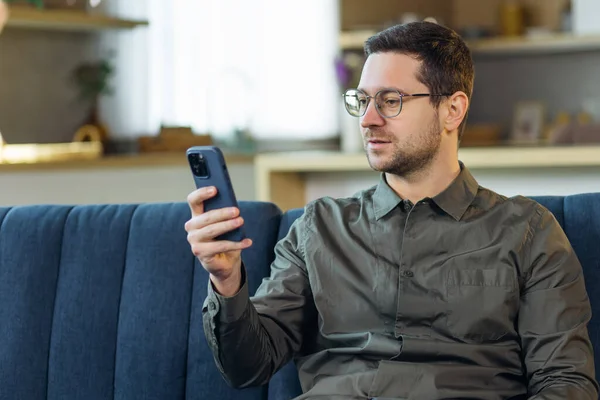 Evdeki Kanepede Oturan Yakışıklı Adam Akıllı Telefon Kullanıyor Video Seyrediyor — Stok fotoğraf